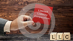 Business hand holding a note with LLC text, the acronym of Limited Liability Company with a row of wooden cubes with LLC text