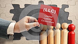 Business hand holding a note with LLC text, the acronym of Limited Liability Company with a row of wooden peg dolls