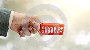 Business hand holding a wooden block with 'sense of urgency' text