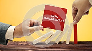 Business hand stopping a falling wooden dominoe with risk management text on the note