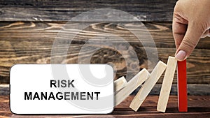 Business hand stopping a falling wooden dominoes with risk management text on the mobile phone screen