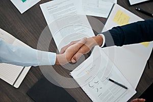 Business, hands and handshake with documents above paperwork for employment agreement or analysis at the office. Hand of