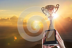 Business hands holding trophy cup on sky background.