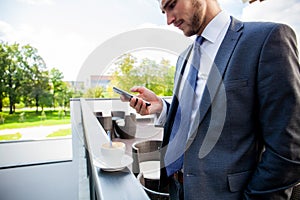 Business, hot drinks and people and concept - young serious businessman with paper coffee cup over office building.