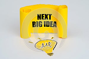 A light bulb is drawn on a white background, next to it is a yellow plate with the inscription - Next Big Idea