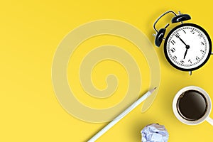 Top view of coffee cup, white pencil, retro alarm clock and white crumpled paper ball place on yellow floo photo