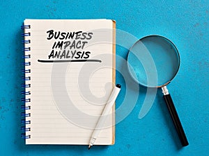 Business impact analysis handwritten on a notebook with a magnifying glass