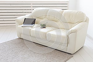 Business and interior concept - view of a white living room with sofa, an open laptop computer, home interior