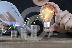 Business investment gains and growth in savings and plan. holding light bulb and virtual graph enhanced by stacking silver coins