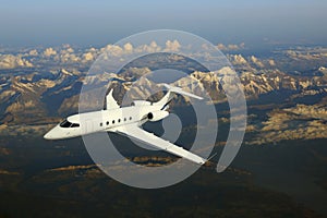 Business jet airplane flying over mountains.