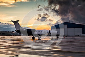 Business jet at sunset after the rain on the airport apron near the hangar