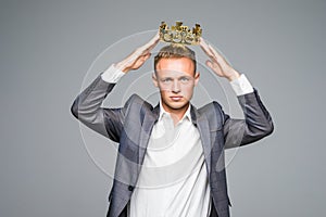 Business king. Confident businessman in crown standing on gray