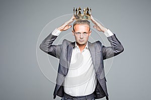 Business king. Confident businessman in crown standing isolated on gray