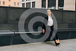 A business lady in a black, stern suit sits on a bench outside work at lunchtime. Customer`s waiting concept