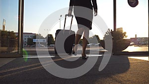 Business lady going to the airport with her luggage. Young woman in heels entering walking through glass doors to the