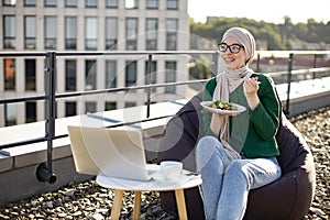 Business lady in headscarf having snack on flat roof at work