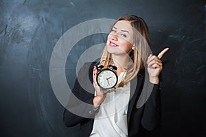 Business lady holding alarm clock with blackboard on background