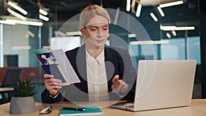 Business lady sitting at workplace with passport and flight tickets in hands.