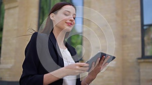 Business lady using tablet outdoors. Smiling woman greeting colleague on street.