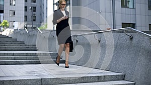 Business lady walking down stairs and texting on smartphone, careerist lifestyle