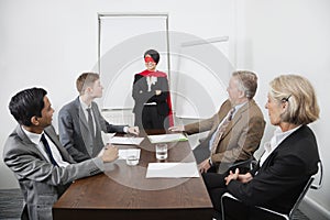 Business leader as superhero in front of colleagues at meeting in conference room