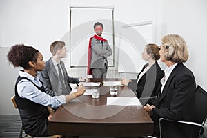 Business leader as superhero in front of colleagues at meeting in conference room
