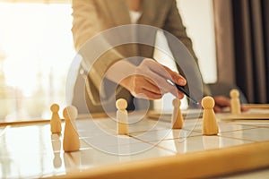 Business leader choosing and pointing at one of wooden people from a group of employees on a planning board