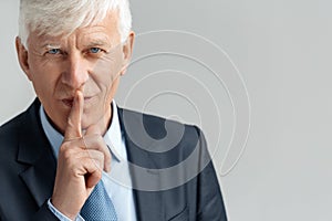 Business Lifestyle. Businessman standing on gray showing secret gesture looking camera playful close-up