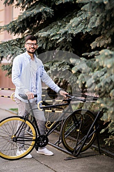 Business, lifestyle, transport and people concept. Young man parking bicycle on city street