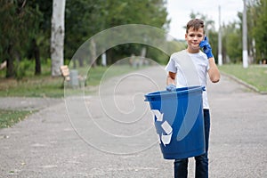 A business-like teenage boy holding a blue recycling bin and speaking on a phone on a blurred natural background.