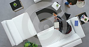 Business lounge and designer woman on tablet working while drinking beverage on sofa with top view. Digital design