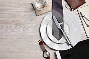 Business lunch concept. Plates, cutlery, glass of water, tie and watch on wooden table, flat lay with space for text