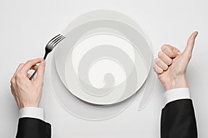 Business lunch and healthy food theme: man's hand in a black suit holding a white empty plate and shows finger gesture on an