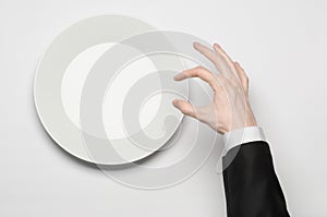 Business lunch and healthy food theme: man's hand in a black suit holding a white empty plate and shows finger gesture on an