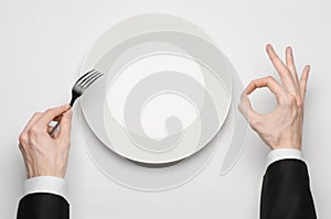 Business lunch and healthy food theme: man's hand in a black suit holding a white empty plate and shows finger gesture on an