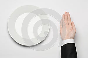 Business lunch and healthy food theme: man's hand in a black suit holding a white empty plate and shows finger gesture on an