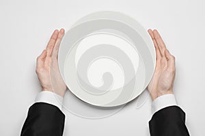 Business lunch and healthy food theme: man's hand in a black suit holding a white empty plate and shows finger gesture on an