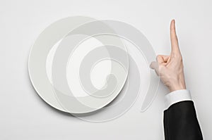 Business lunch and healthy food theme: man's hand in a black suit holding a white empty plate and shows finger gesture on an