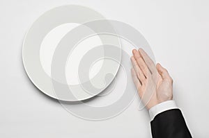 Business lunch and healthy food theme: man's hand in a black suit holding a white empty plate and shows finger gesture on an