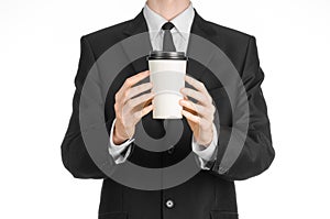 Business lunches coffee theme: businessman in a black suit holding a white blank paper cup of coffee with a brown plastic cap isol