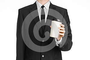 Business lunches coffee theme: businessman in a black suit holding a white blank paper cup of coffee with a brown plastic cap isol