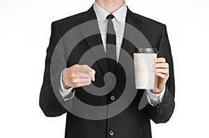 Business lunches coffee theme: businessman in a black suit holding a white blank paper cup of coffee with a brown plastic cap isol