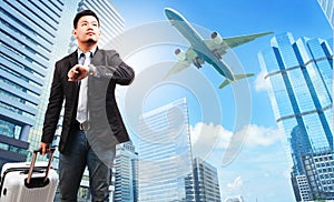 business man and belonging luggage watching to sky and hand watch against high building skyscrapers and passenger plane flying ab