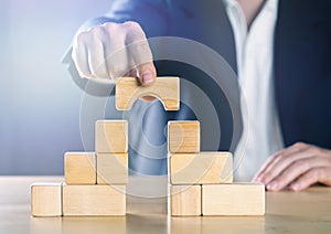 Business man bridging the gap between two towers or parties made from wooden blocks; conflict management or mediator concept photo