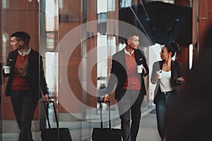 Business man and business woman talking and holding luggage traveling on a business trip, carrying fresh coffee in their