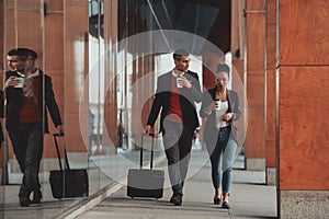 Business man and business woman talking and holding luggage traveling on a business trip, carrying fresh coffee in their