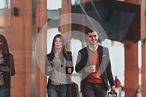 Business man and business woman talking and holding luggage traveling on a business trip, carrying fresh coffee in their