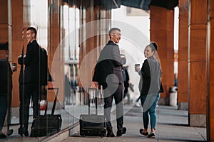 Business man and business woman talking and holding luggage traveling on a business trip, carrying fresh coffee in their