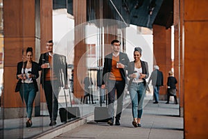 Business man and business woman talking and holding luggage traveling on a business trip, carrying fresh coffee in their