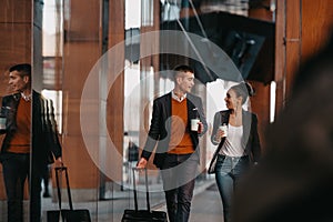 Business man and business woman talking and holding luggage traveling on a business trip, carrying fresh coffee in their